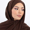 Une femme portant un hijab en mousseline instantanée marron uni, regardant sur le côté.