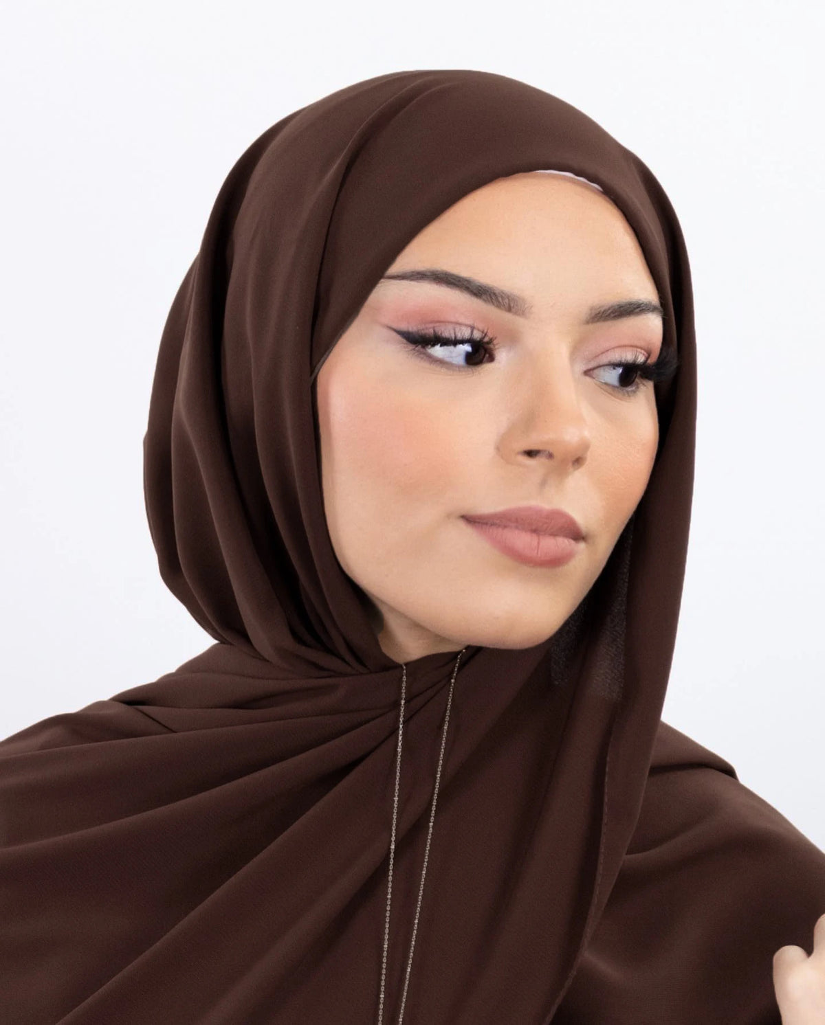 Une femme portant un hijab en mousseline instantanée marron uni, regardant sur le côté.