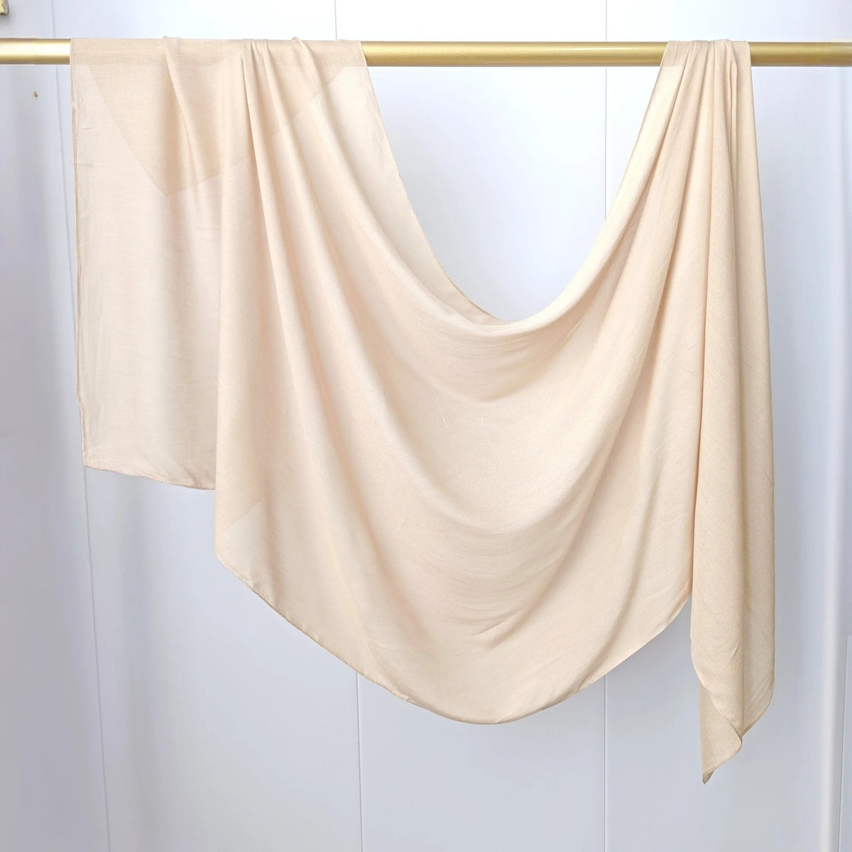 Écharpe de hijab beige uni drapée sur un cintre doré.