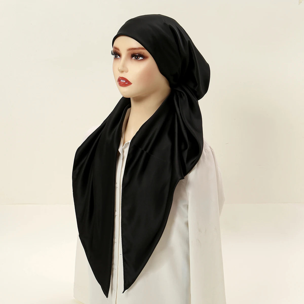 A woman models a black satin silk instant hijab scarf draped over her head and neck, paired with a white top.