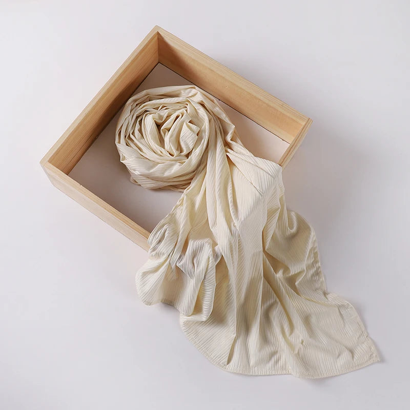 A cream ribbed jersey hijab scarf is draped within a light wooden frame.