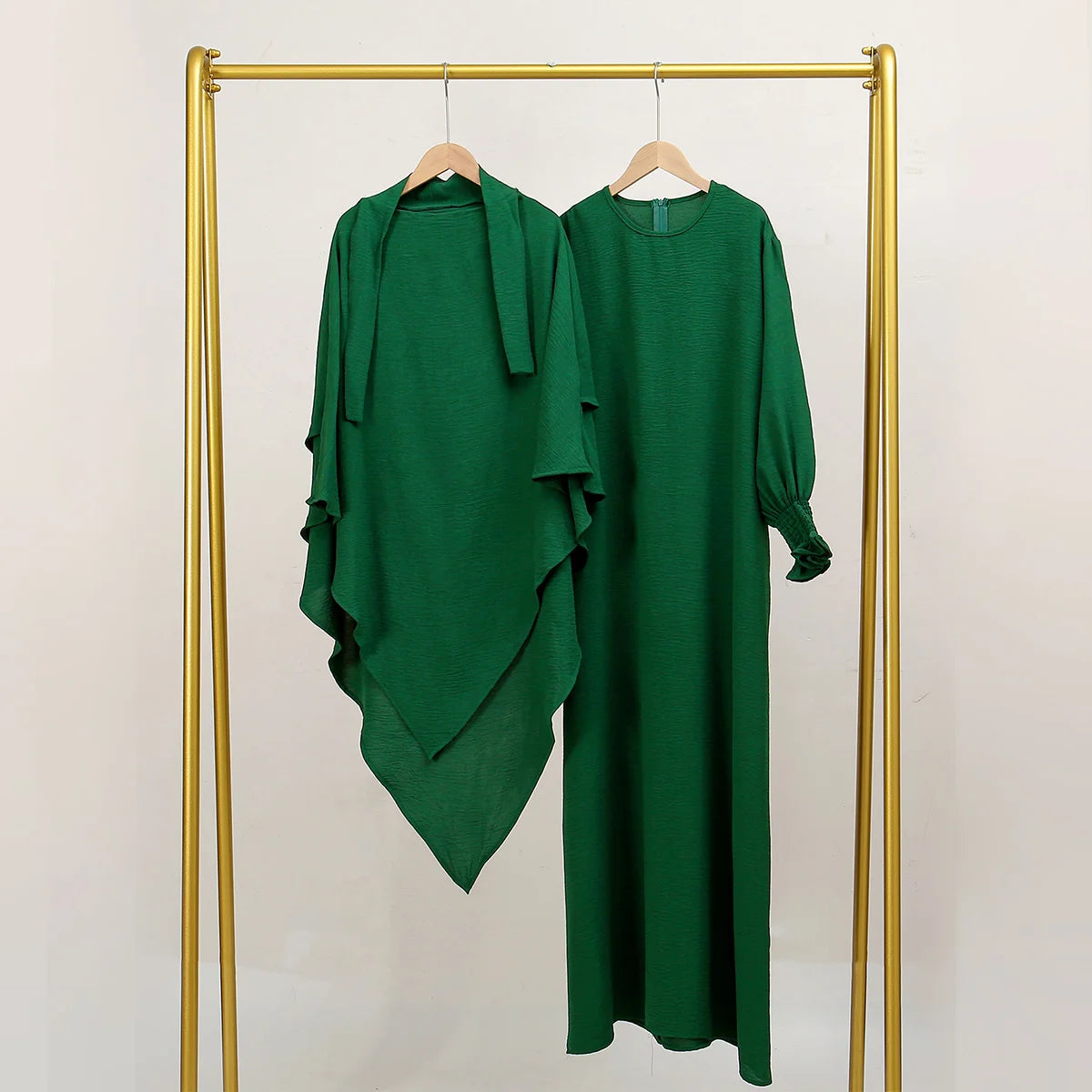 A deep emerald green abaya and khimar set displayed on a gold hanger against a white background.