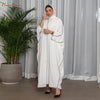 Una mujer vistiendo una abaya blanca oversize con ribetes negros y un cinturón a juego, de pie en interiores.