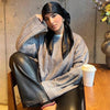 A woman wearing a solid color silk satin hijab scarf and black leather pants sitting at a wooden table.