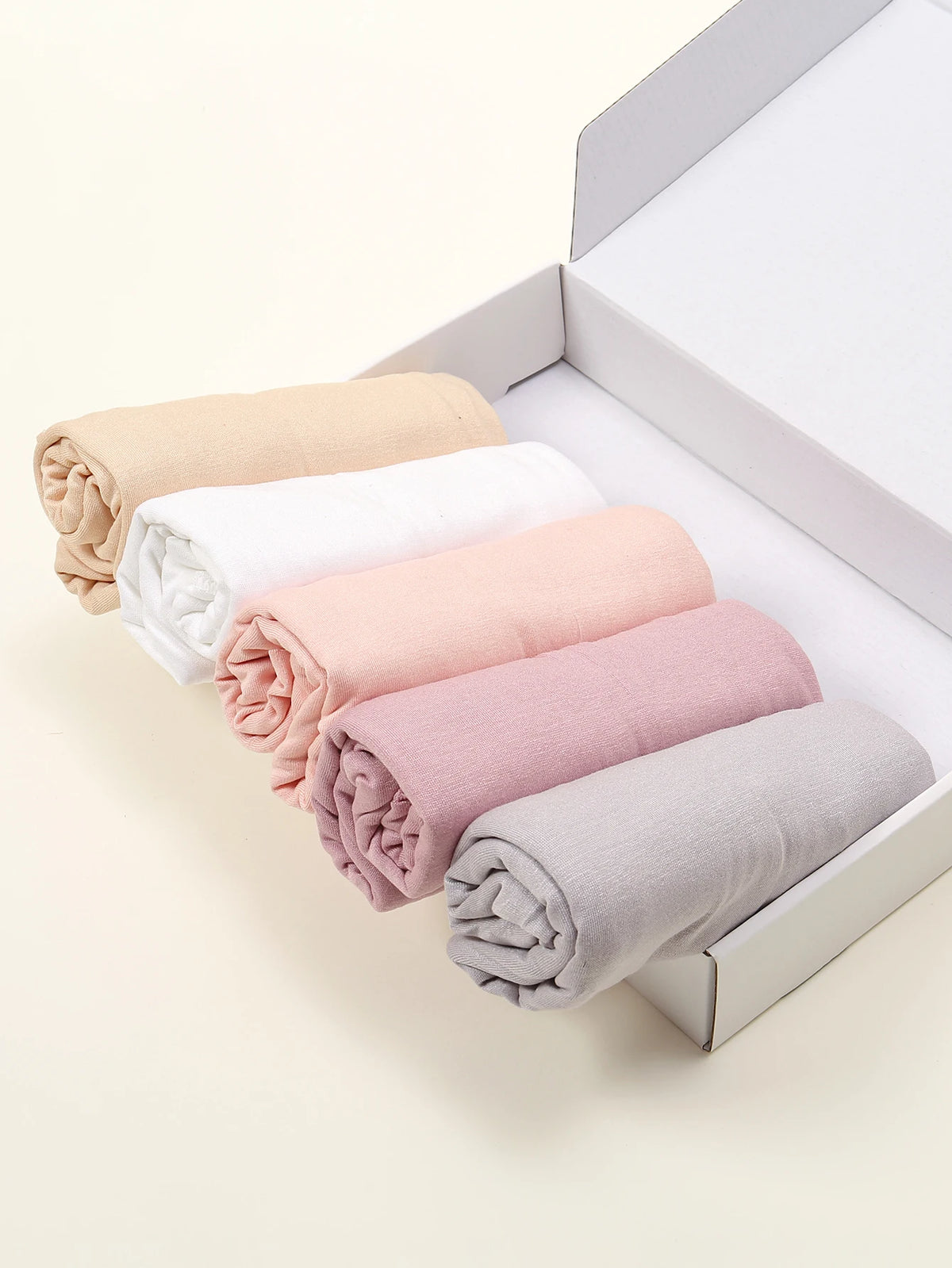 Ein Set von fünf einfarbigen Jersey-Hijab-Schals in Beige, Weiß, Pink und Grau, ordentlich gefaltet in einer weißen Box.