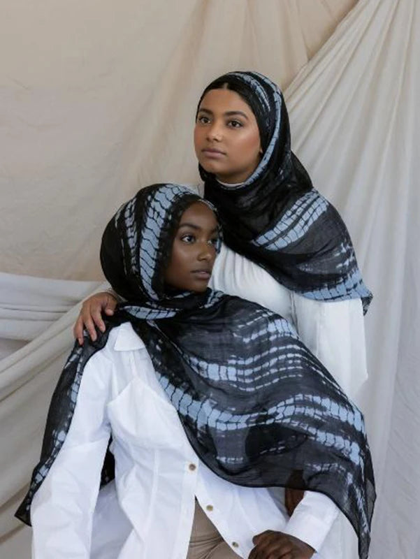 Una mujer vistiendo un pañuelo hijab con estampado de leopardo acuarela negro y gris y una camisa blanca, posando contra un f