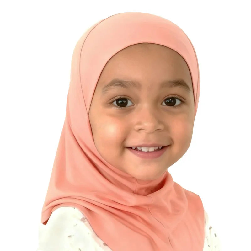 Niña sonriente vistiendo un pañuelo instantáneo musulmán de color melocotón.