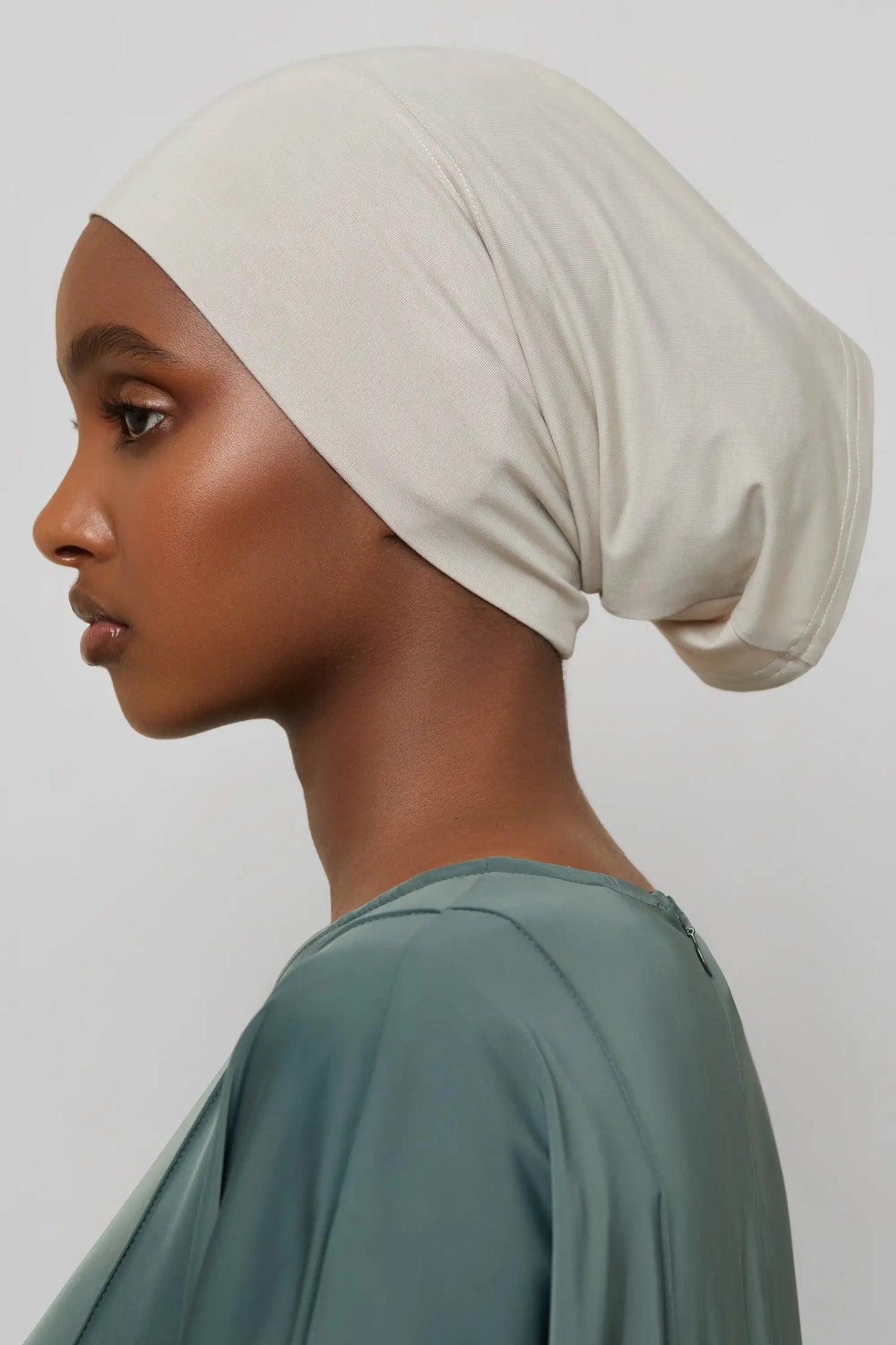 Model wearing a beige bamboo jersey tube hijab cap and a sage green top.
