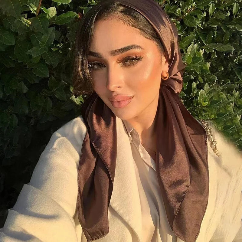 A woman wearing a brown silk satin hijab scarf and a white coat, looking directly at the camera.
