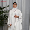 Una mujer vistiendo una abaya blanca oversize con ribetes marrones y un hiyab a juego, de pie en interiores.