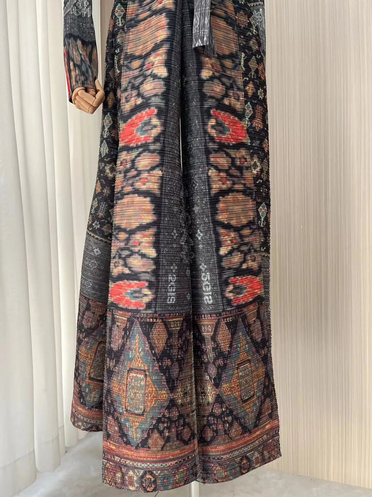 Trench-coat plissé noir et orange à motifs, manches longues et drapées verticalement.
