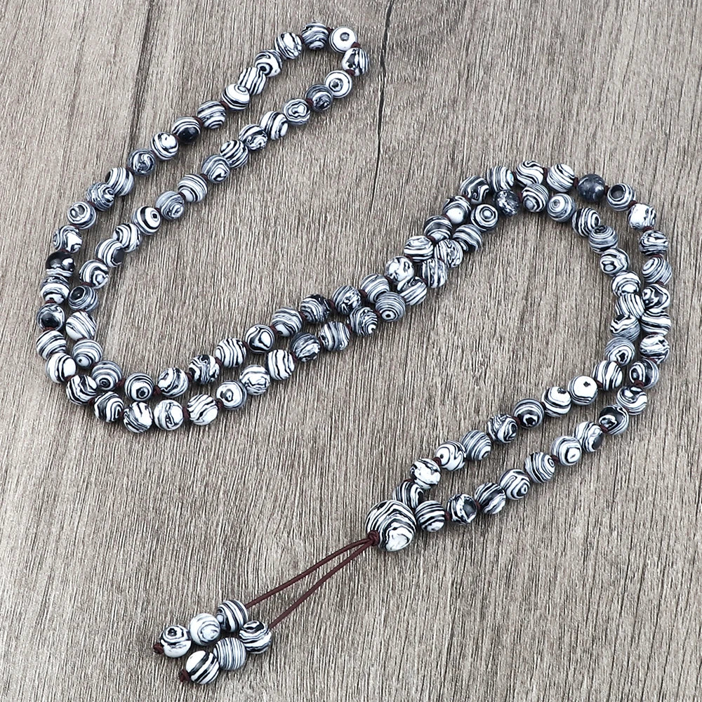 Silber- und schwarze Natursteinperlenkette mit strukturierten sphärischen Perlen auf Holzoberfläche.