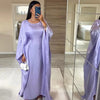 Una mujer vistiendo una abaya de satén lila tipo batwing está de pie frente a un espejo.