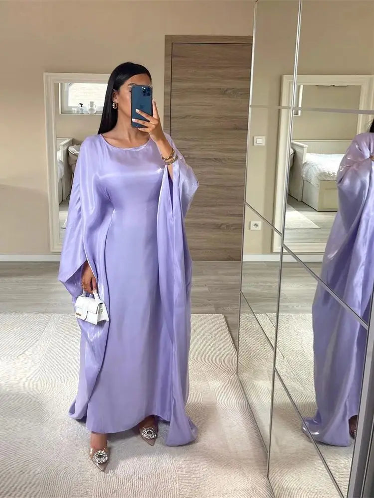 Una mujer vistiendo una abaya de satén lila tipo batwing está de pie frente a un espejo.
