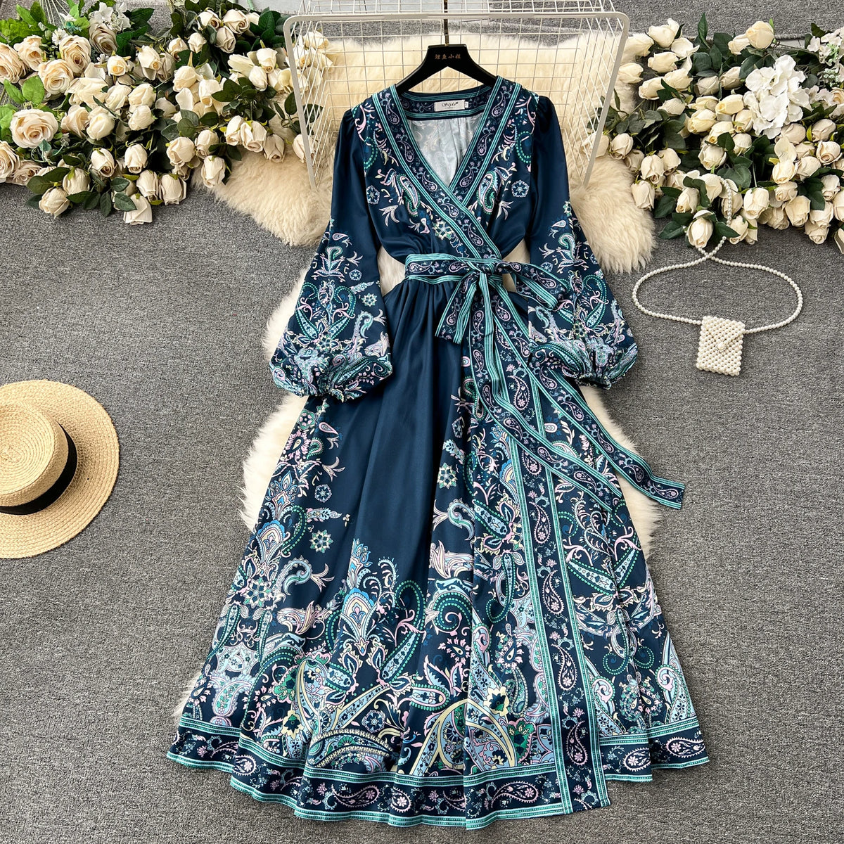 Dunkelblaue Blumenspitze Maxi-Kleid mit aufwendiger Stickerei, präsentiert auf einem Bügel umgeben von weißen Blumen und Pelz