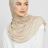Eine Frau trägt einen beige Jersey-Hijab und ein weißes Oberteil.