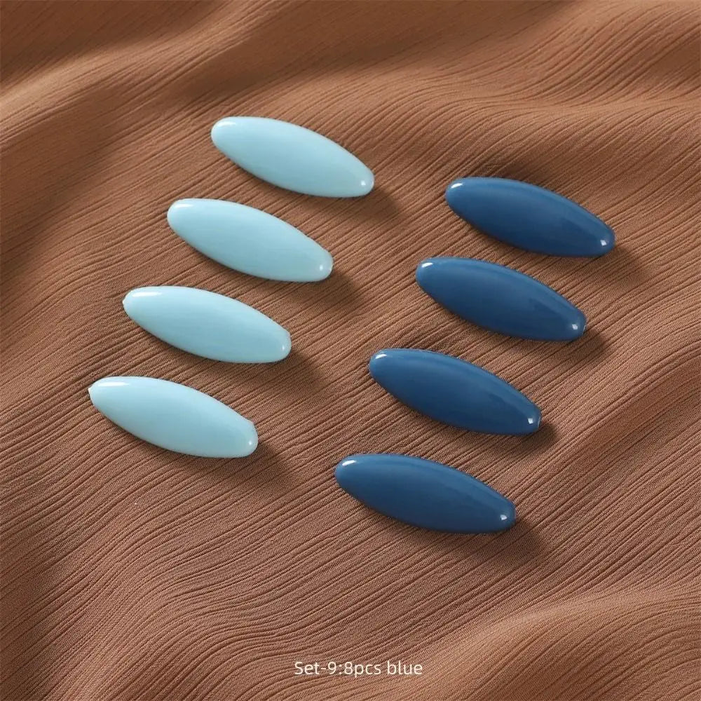Eight oval blue brooch pins arranged on a brown fabric background.