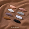 Set of 8 solid color brooch pins in various shades including pink, white, purple, and black on a brown fabric background