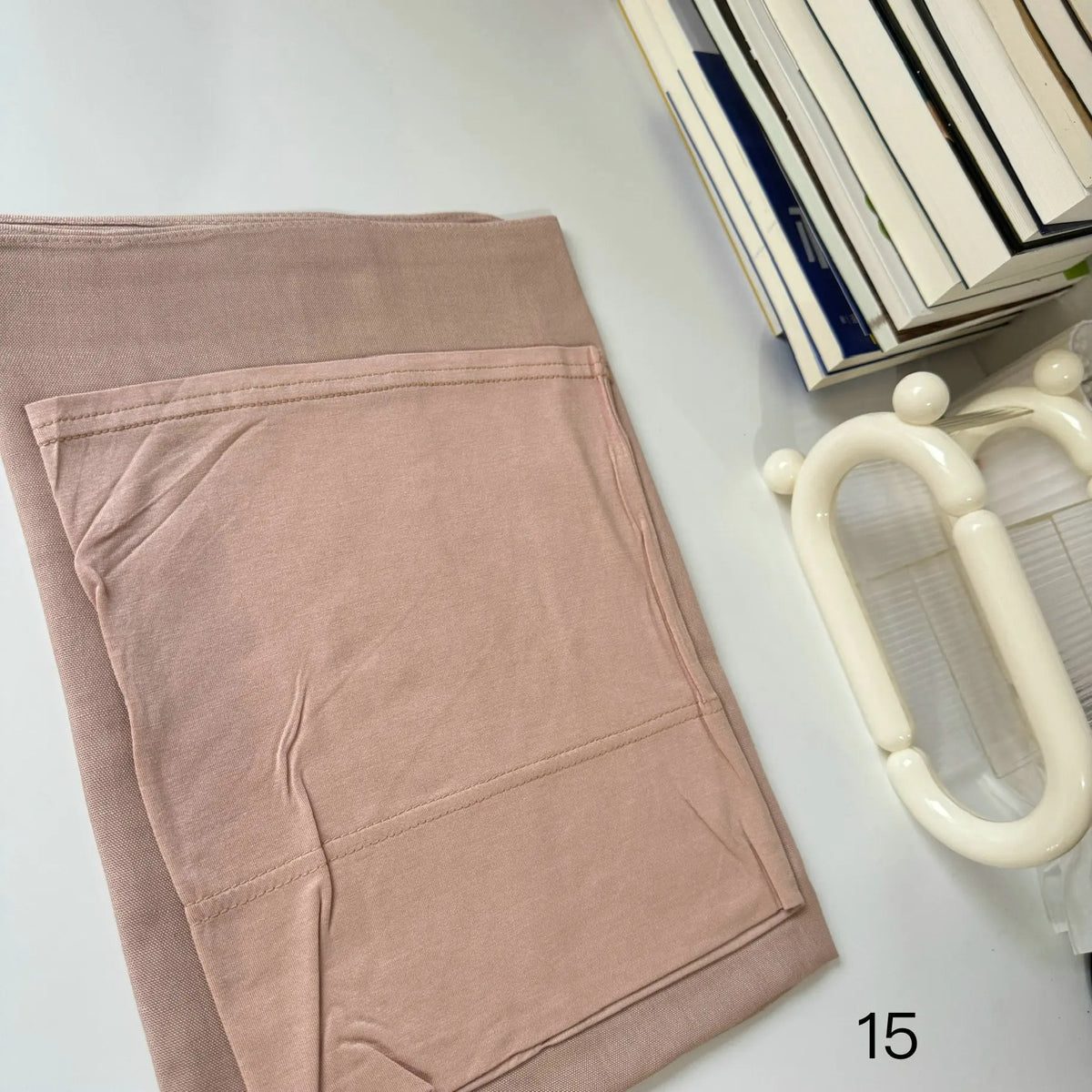 A light pink soft modal rayon hijab set laid out next to a stack of books and a white plastic accessory.