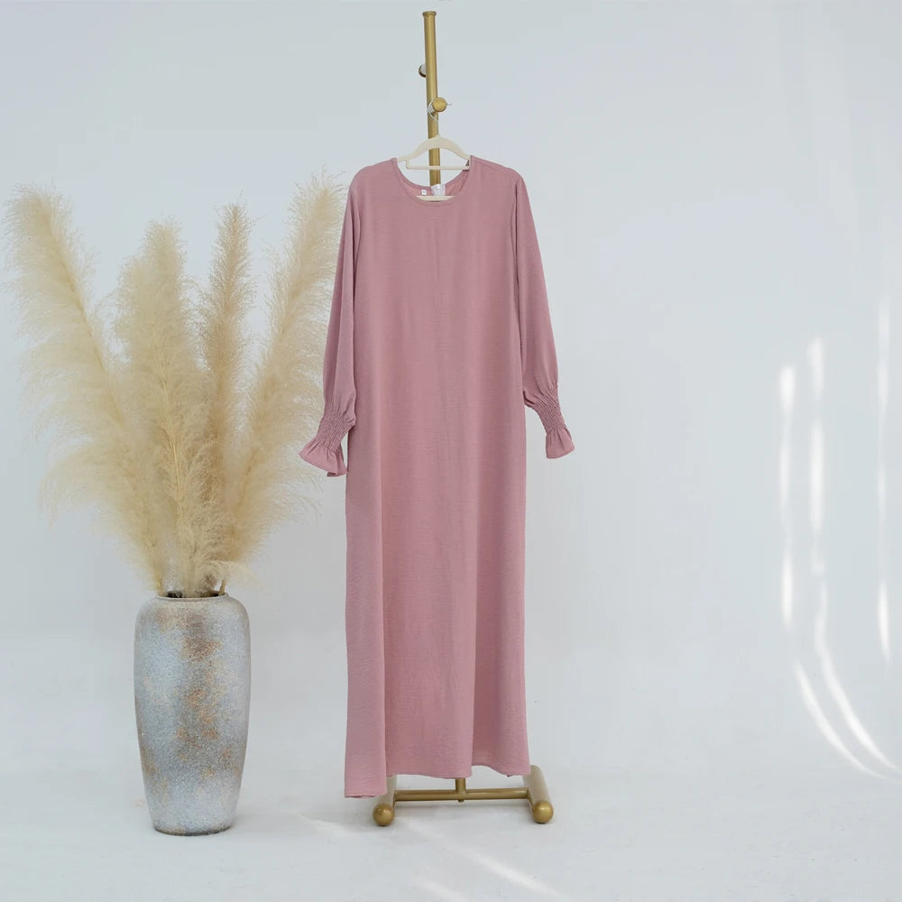 Vestido abaya oversize color rosa empolvado colgado en percha de madera contra fondo blanco.