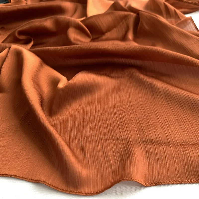 Nahaufnahme von rostorangefarbenem, gekräuseltem Satin-Chiffon-Hijabstoff, drapiert und gefaltet.