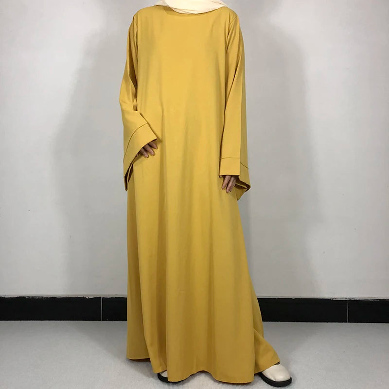 Une longue robe abaya jaune moutarde simple avec une ceinture et un foulard beige clair.