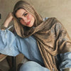 Una mujer vistiendo un pañuelo hijab floral de acuarela bohemio marrón y dorado sobre una camisa azul.
