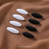 A set of eight solid color brooch pins in black and white are displayed on a brown fabric background.