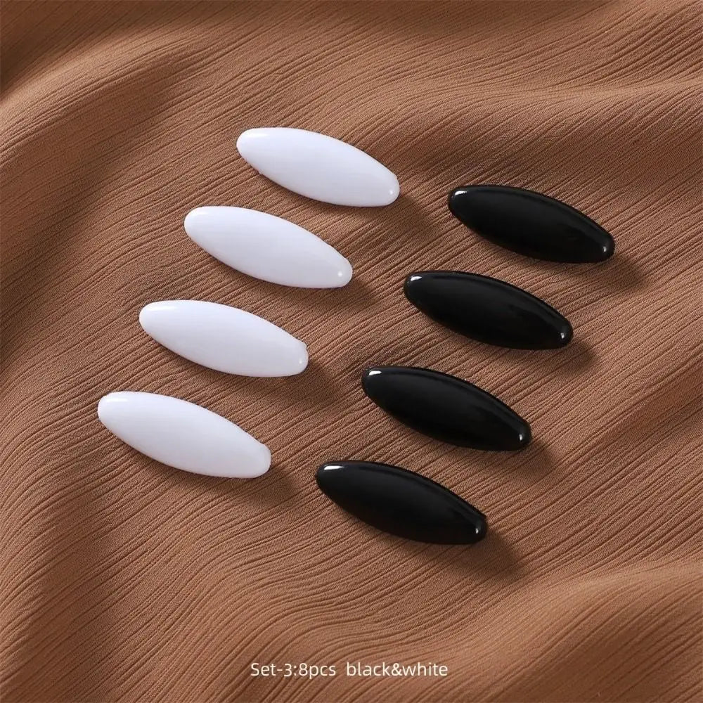 A set of eight solid color brooch pins in black and white are displayed on a brown fabric background.