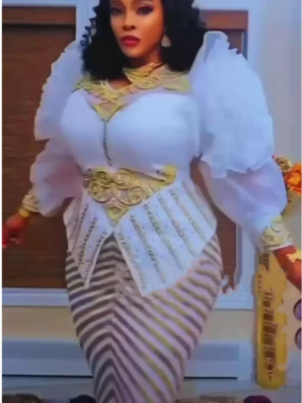 A woman wearing a white and gold sequin African party dress with puffy sleeves and a layered bodice.
