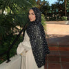 Eine Frau mit schwarzem Hirschmuster-Hijab-Schal und weißem Kleid im Freien.