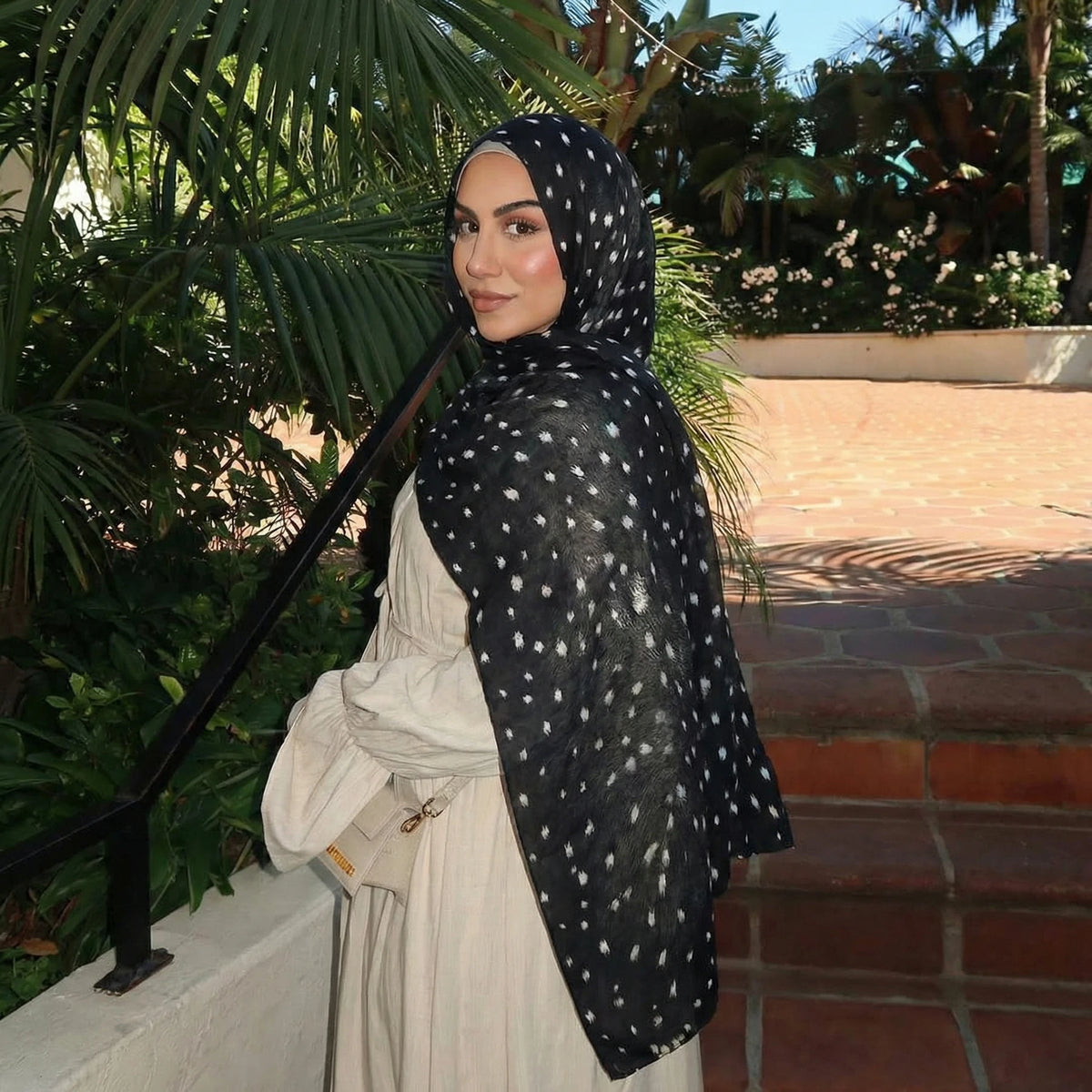 Eine Frau mit schwarzem Hirschmuster-Hijab-Schal und weißem Kleid im Freien.