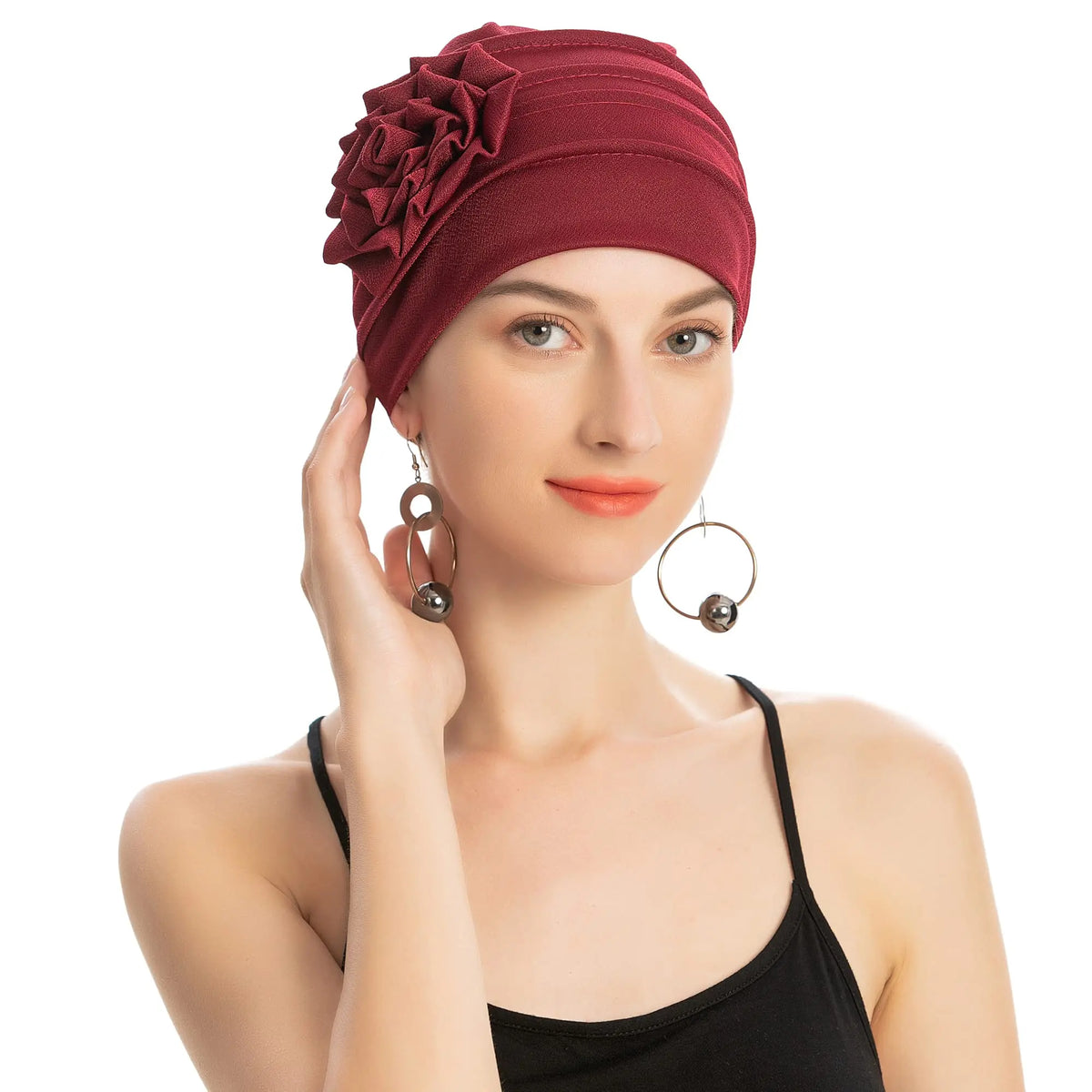 Eine Frau trägt eine tiefrote, floral bestickte Hijab-Turbanmütze und ein schwarzes Tanktop.