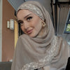 Une femme portant un foulard chiffon beige avec bordure de dentelle à cils, regardant l'appareil photo.