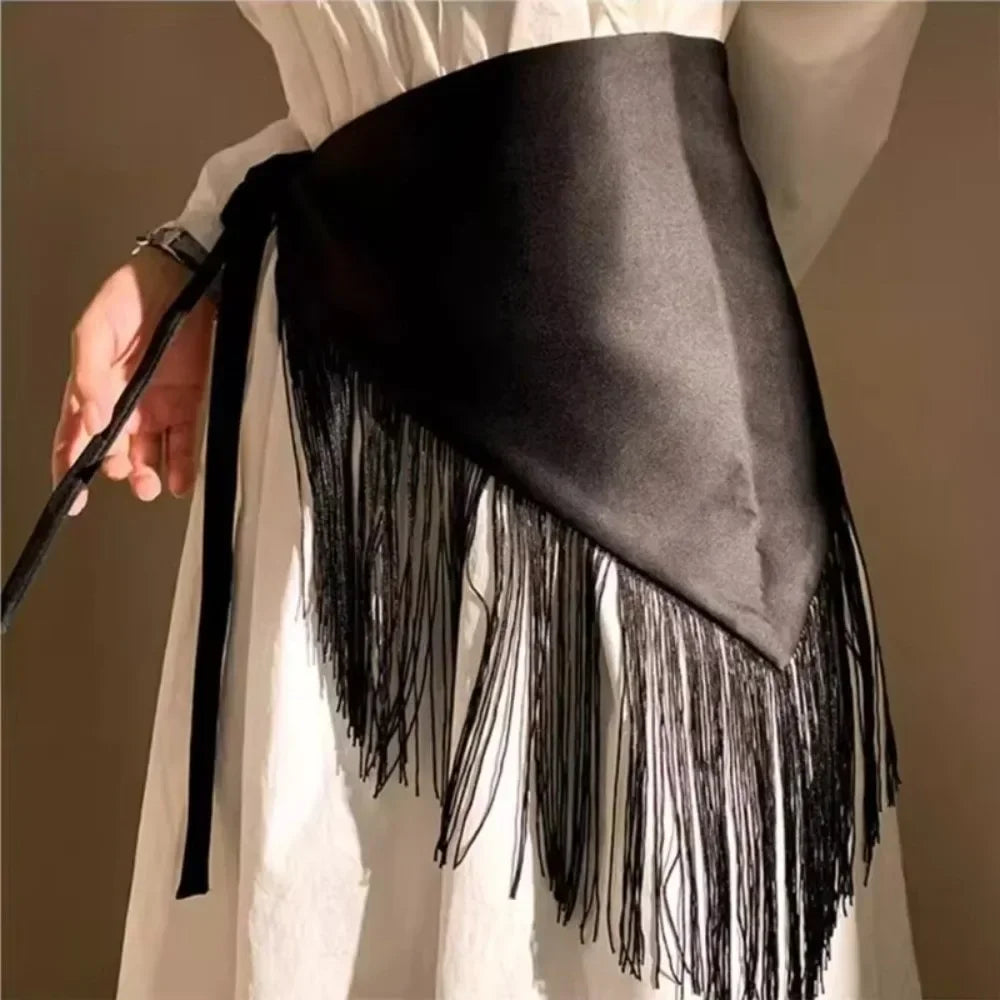 Ceinture triangle en satin noir avec longues pompons noirs portée sur un vêtement blanc.