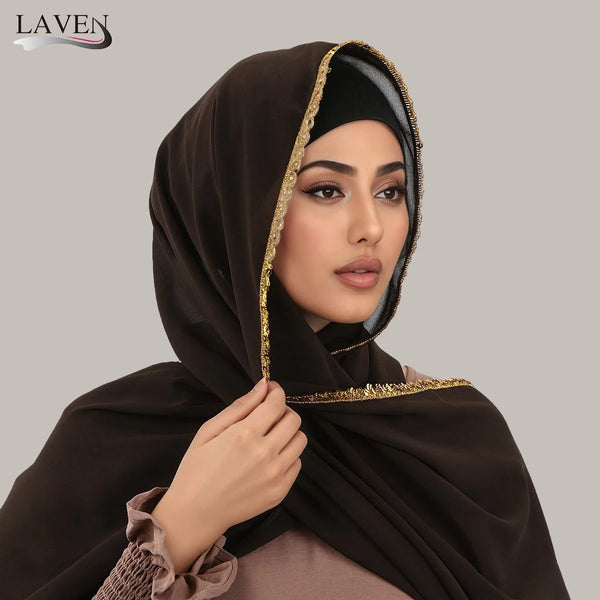 A woman wearing a dark brown chiffon hijab with gold rhinestone trim.