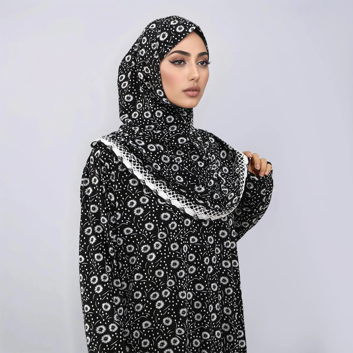 Una mujer vistiendo una abaya de lino floral negra con capucha y turbante, mirando a la cámara.