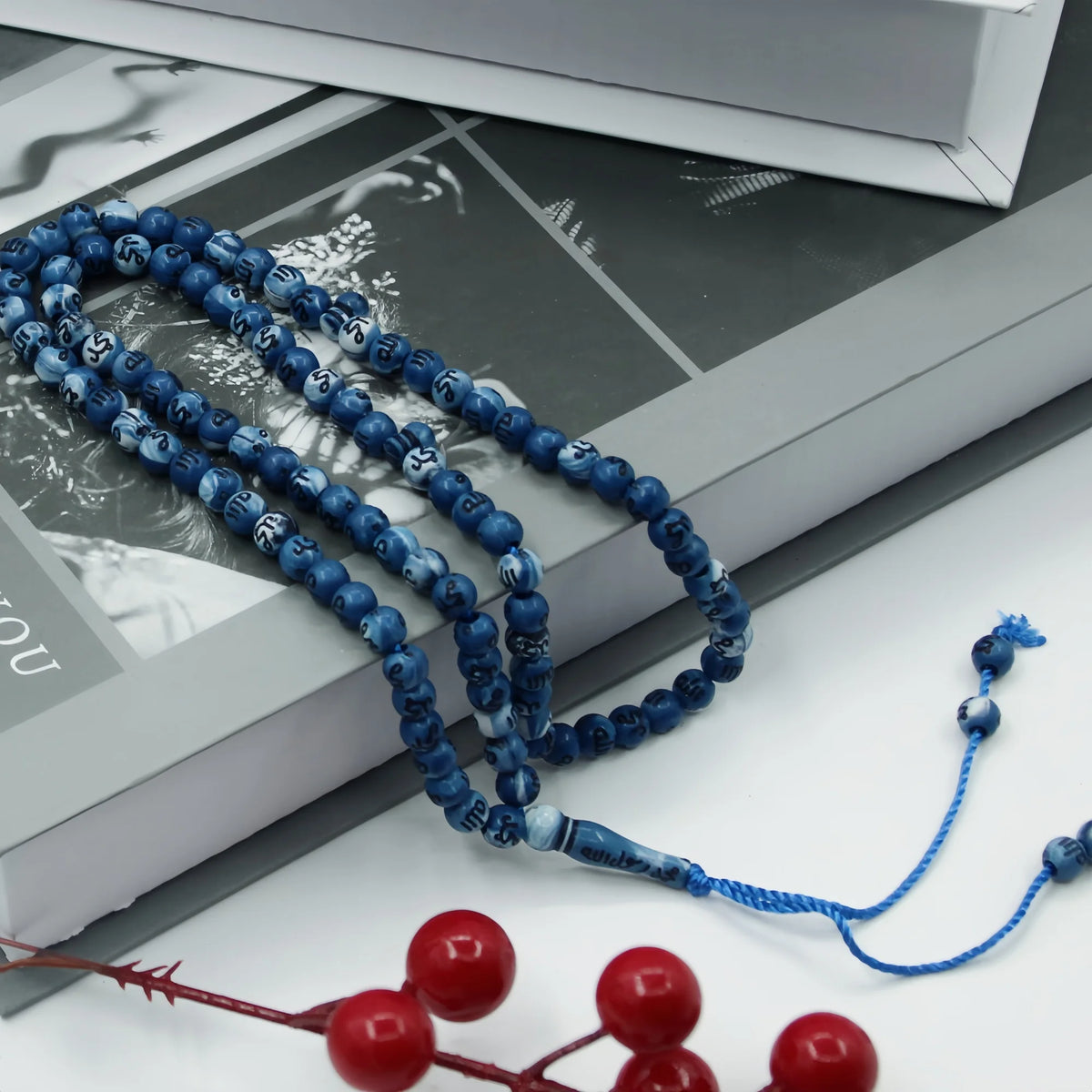 Blue Islamic prayer tasbih beads laid out on a white surface next to an open book.