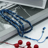 Blue Islamic prayer tasbih beads laid out on a white surface next to an open book.
