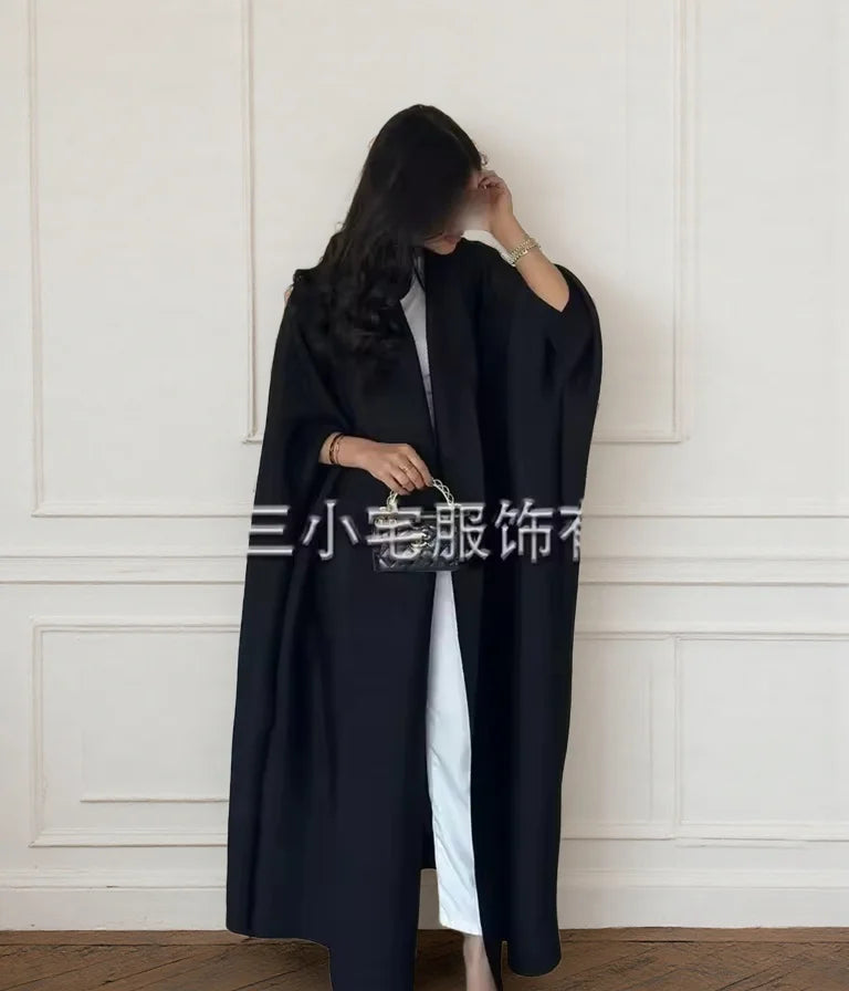 Una mujer vistiendo un cárdigan abaya plisado largo y negro con ropa interior blanca.