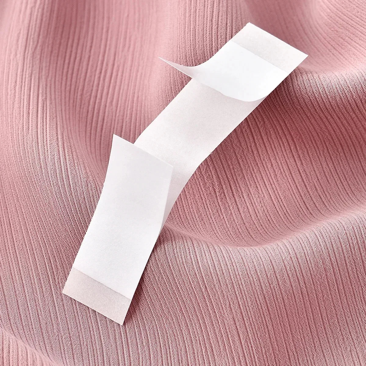 Un rollo de cinta corporal invisible blanca sobre un fondo de tela rosa acanalada.