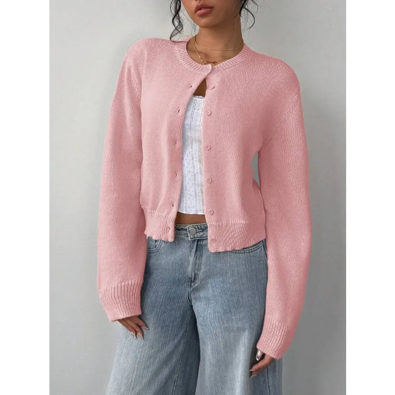 Une femme porte un pull tricoté rose sur un haut blanc et un jean bleu.