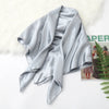 A draped, silky light gray satin scarf or hijab displayed on a white surface next to a fluffy white rug.