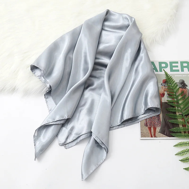 A draped, silky light gray satin scarf or hijab displayed on a white surface next to a fluffy white rug.