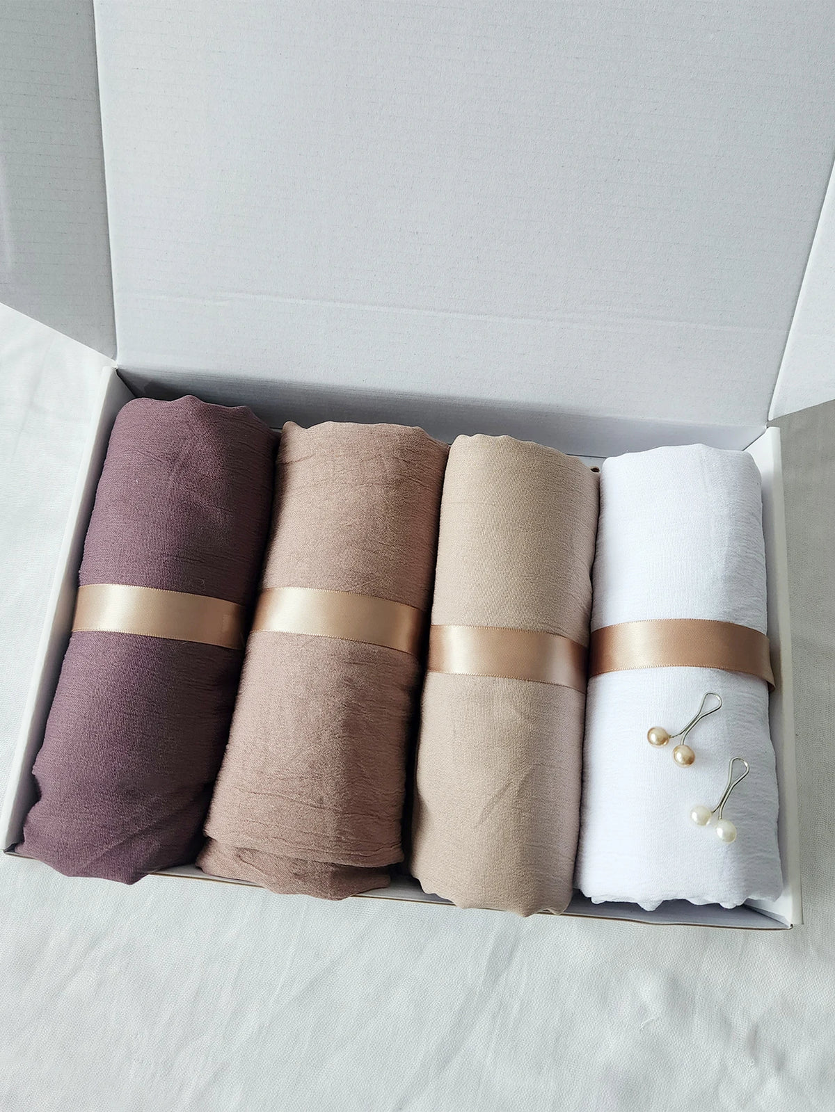 Set von vier zerknitterten Baumwoll-Hijab-Schals in Mauve-, Beige- und Weißtönen, verpackt in einer Kartonbox.