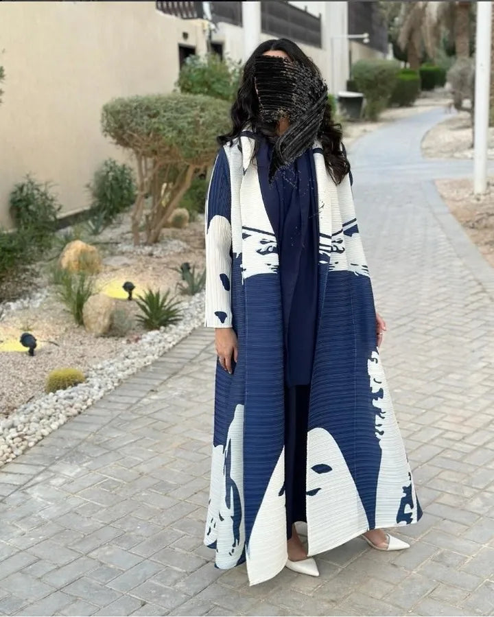 Una mujer vistiendo un cárdigan abaya plisado azul marino con estampado blanco, de pie en una acera pavimentada.