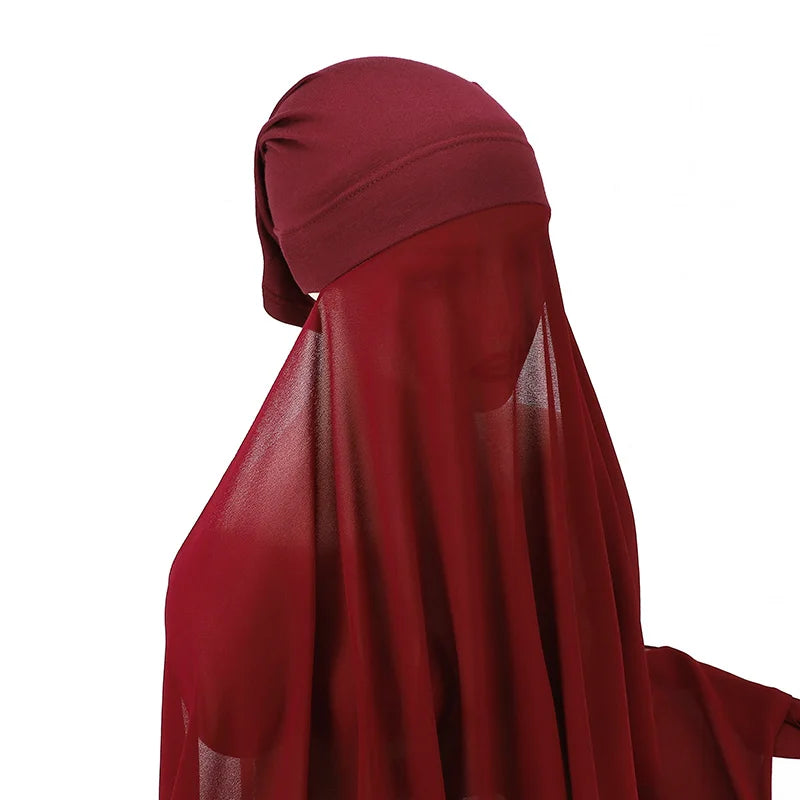Un conjunto de hijab y chal de gasa color granate drapeado sobre la cabeza y los hombros de una persona.