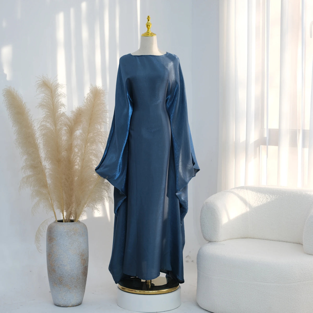 Langes, fließendes, staubbläuliches Kaftankleid auf einem Mannequin neben getrocknetem Pampasgras.