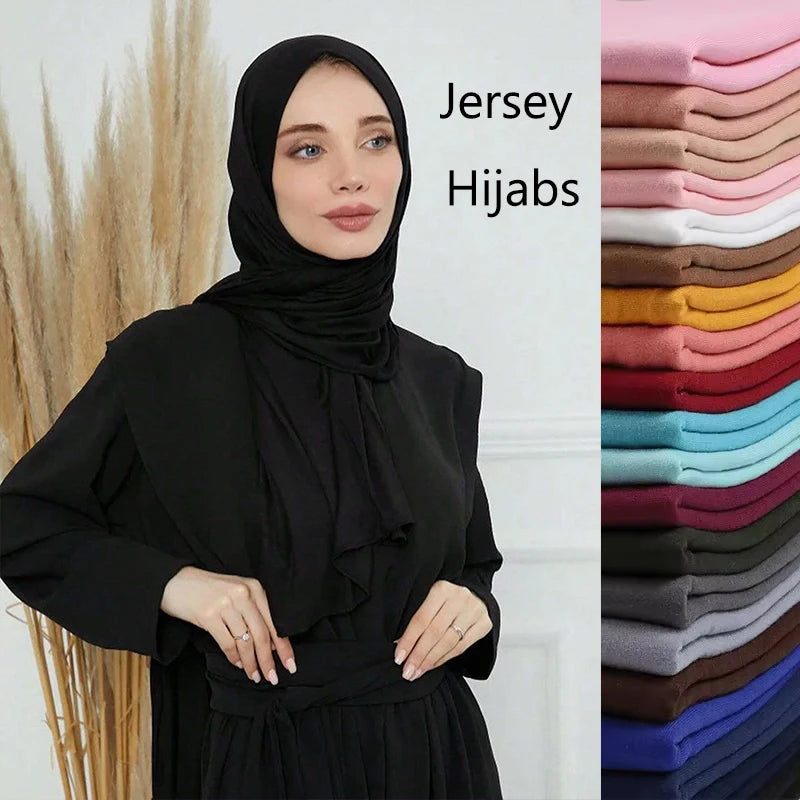 Eine Frau mit schwarzem Jersey-Hijab neben einem Stapel aus 28farbigen Modal-Baumwoll-Jersey-Hijabs.