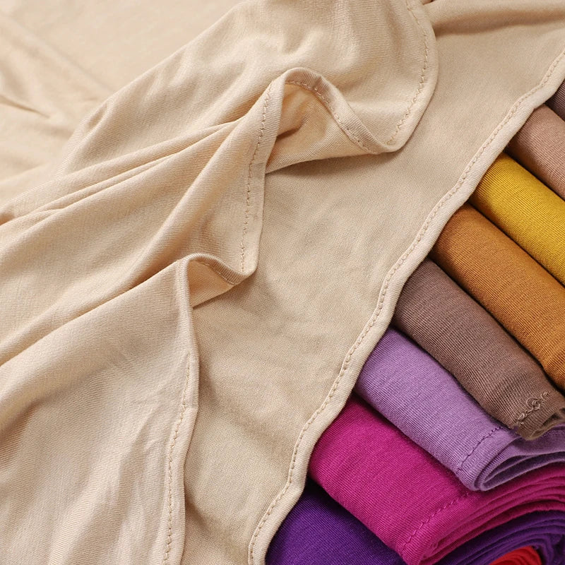 Stapel von weichen Baumwolljersey-Instant-Hijab-Schals in verschiedenen Pastell- und dunklen Farben, gefaltet und drapiert.